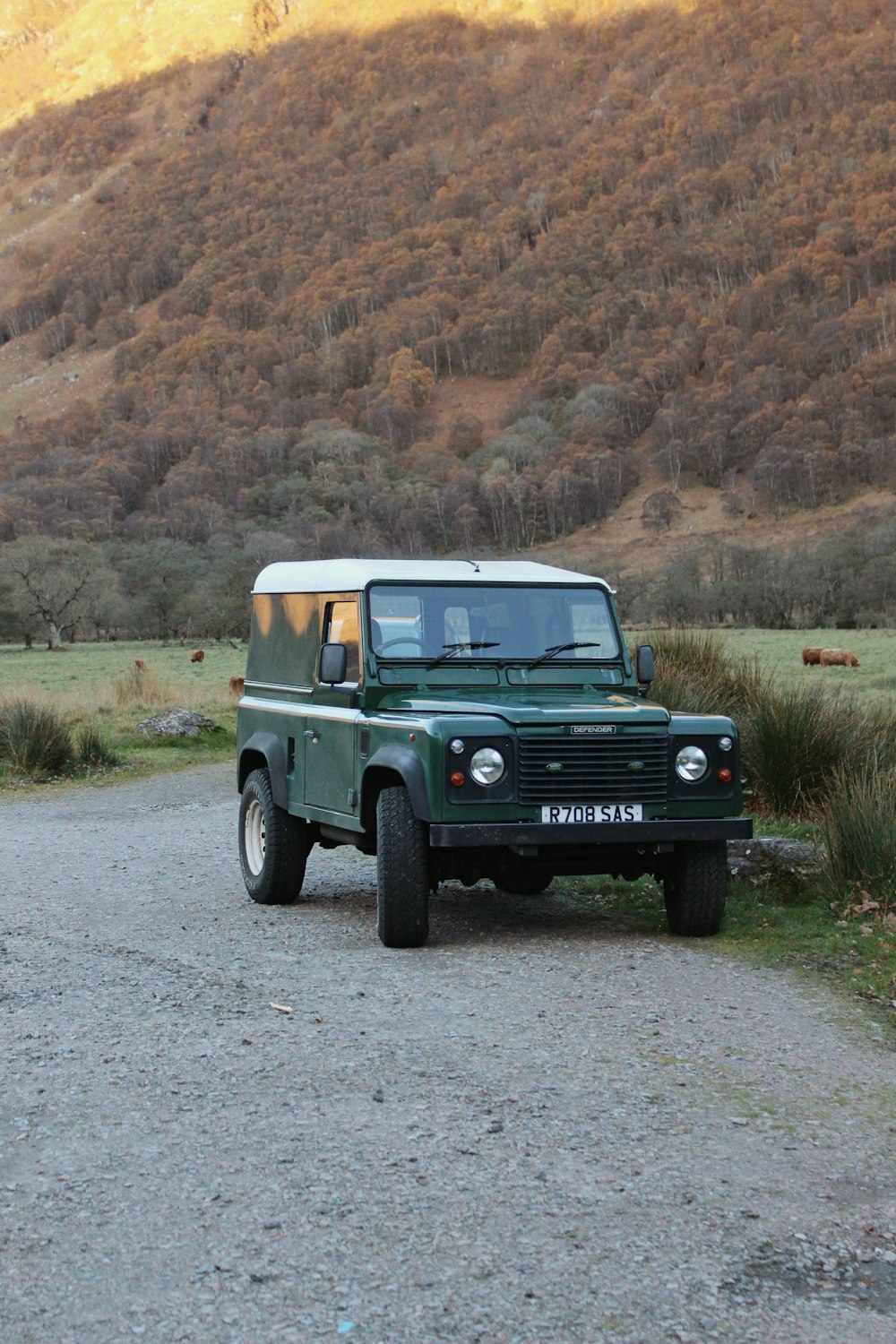 a green land rover is parked on a gravel road