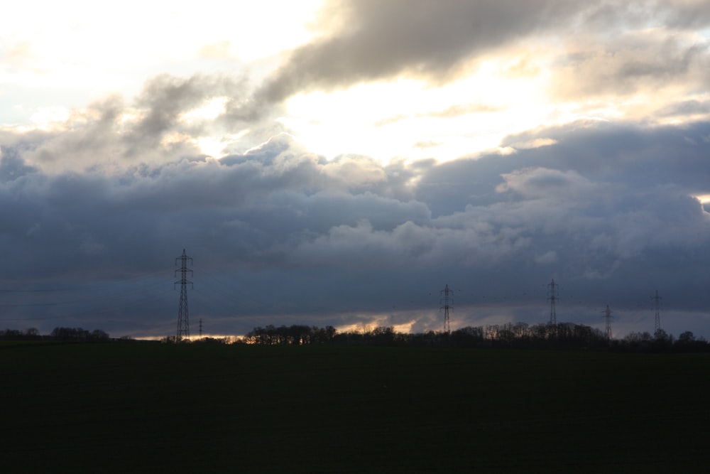 a field with power lines in the distance under a cloudy sky