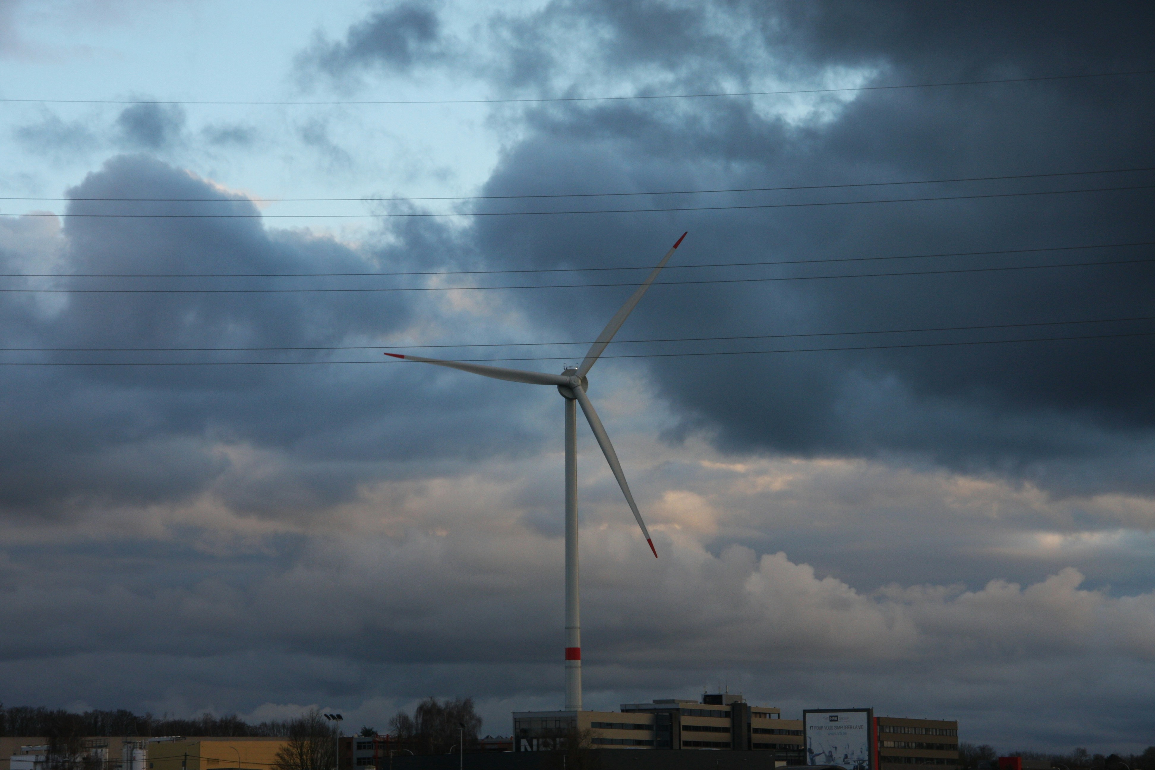 a wind turbine on a cloudy day with power lines in the background