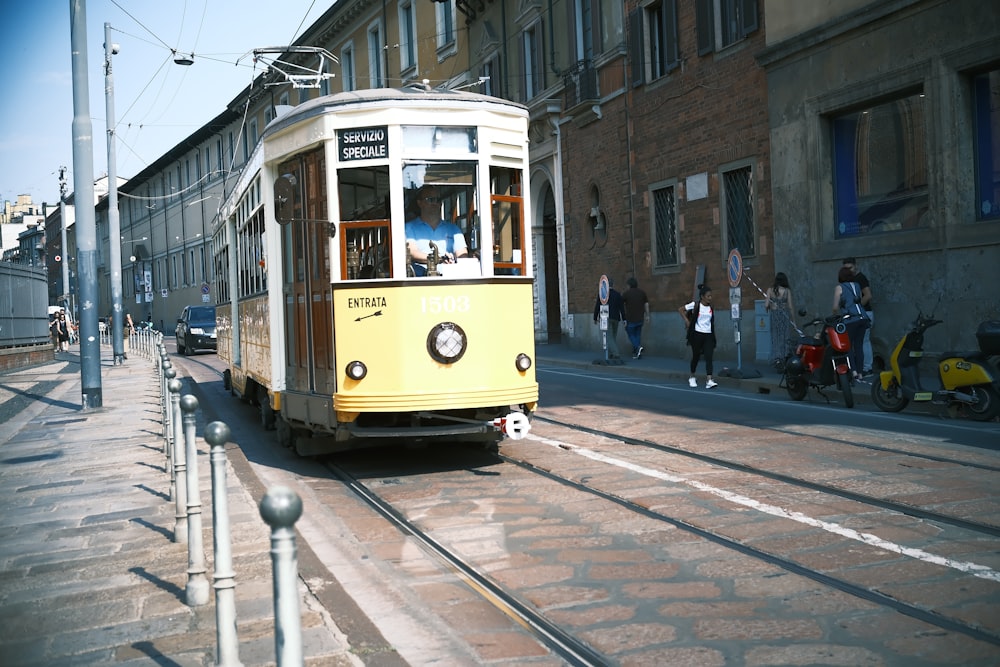 a yellow trolley car traveling down a street next to tall buildings