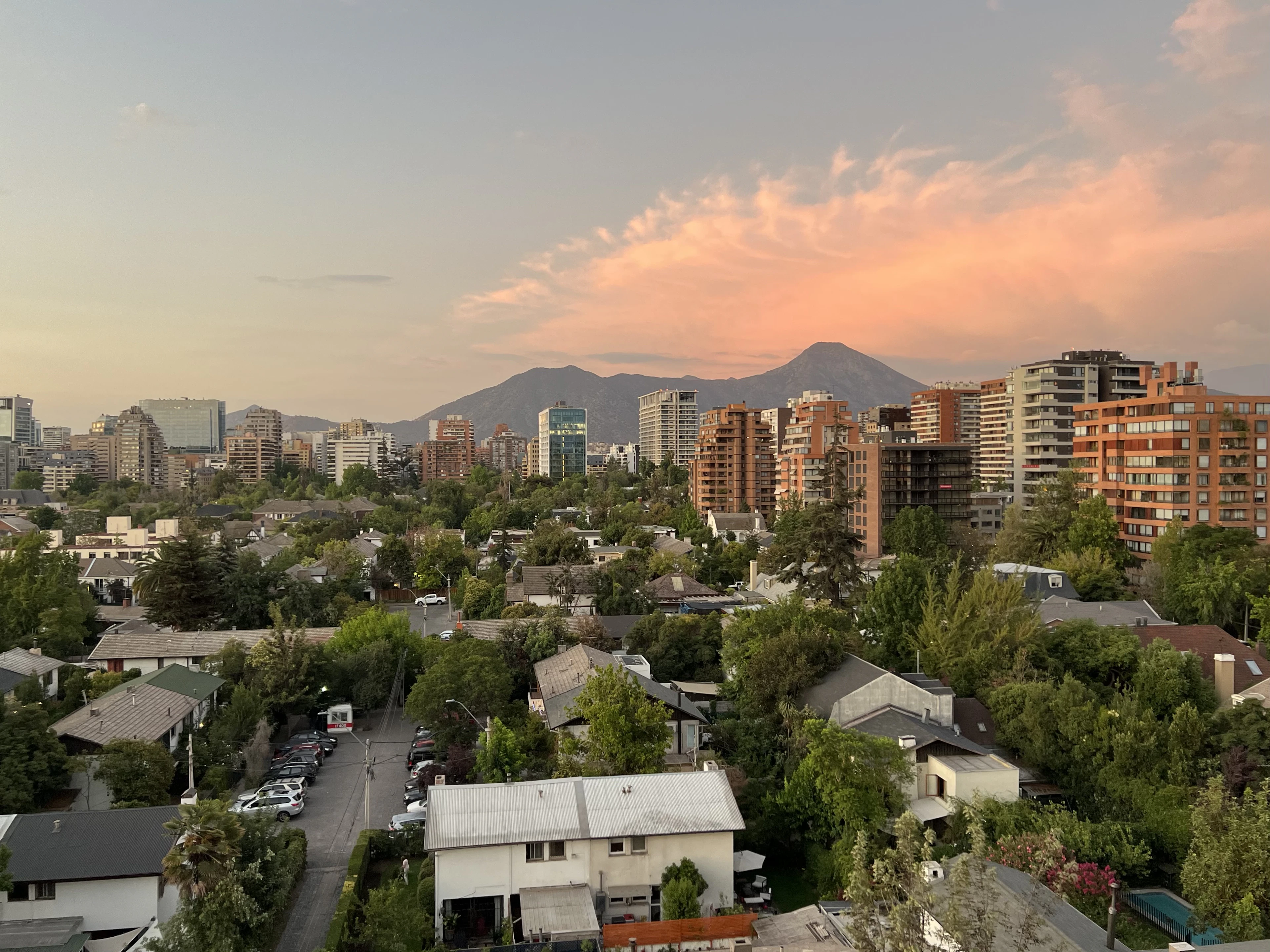 Santiago's tree-lined residential rooftops at dusk, with the Andes glowing pink behind the skyline.