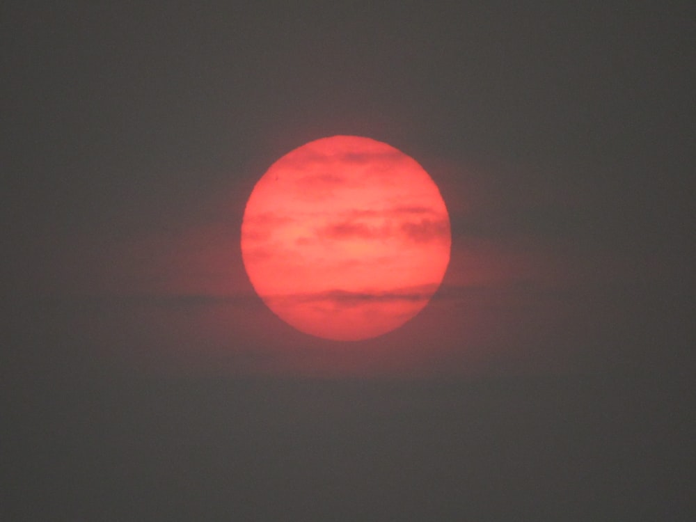 a bright red sun is seen through a foggy sky