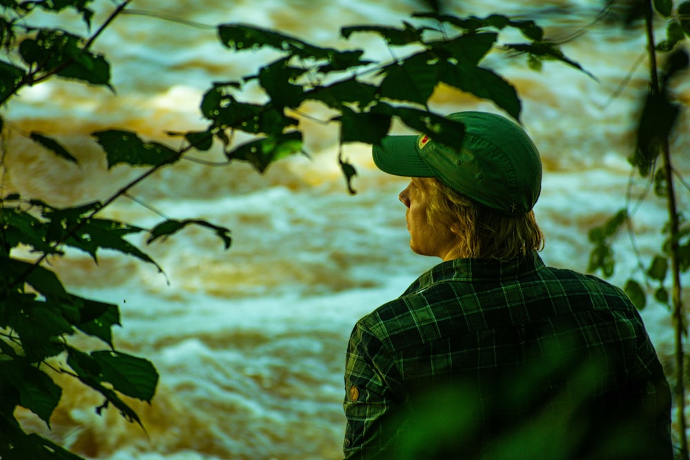 a man wearing a green hat standing in front of a river