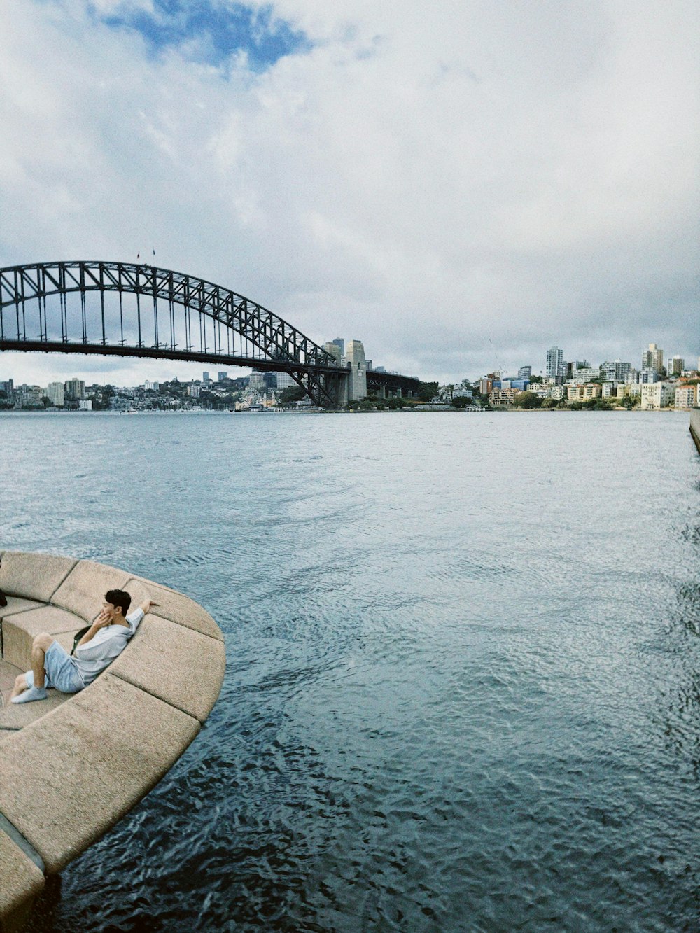 a man sitting on the edge of a boat in front of a bridge