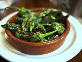 a brown bowl filled with green peppers on top of a white plate