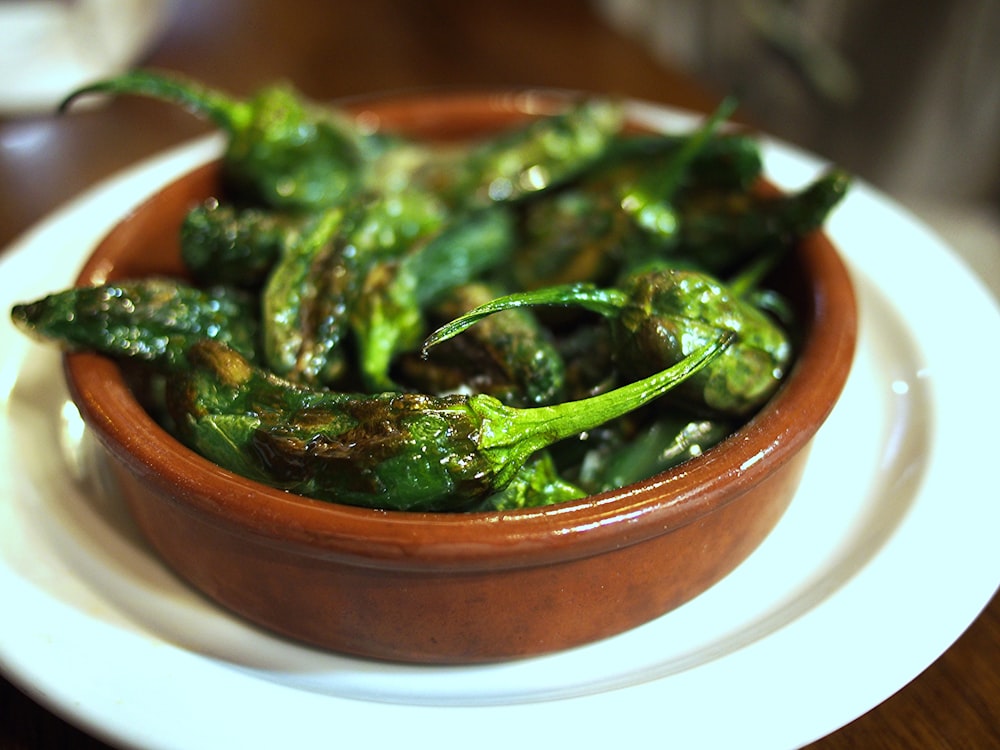 a brown bowl filled with green peppers on top of a white plate