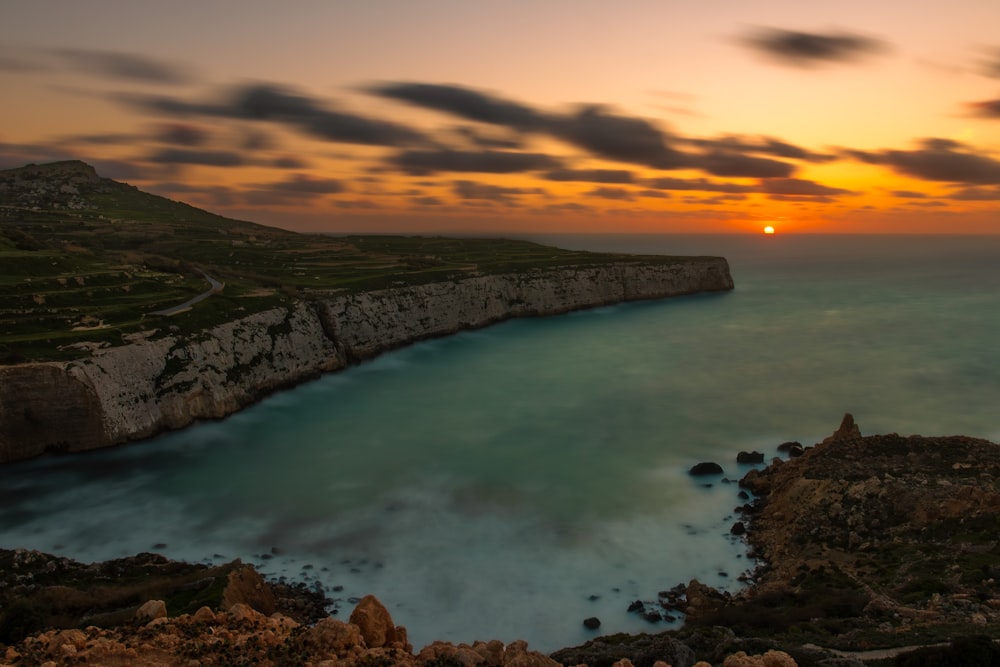 the sun is setting over the ocean near a rocky cliff