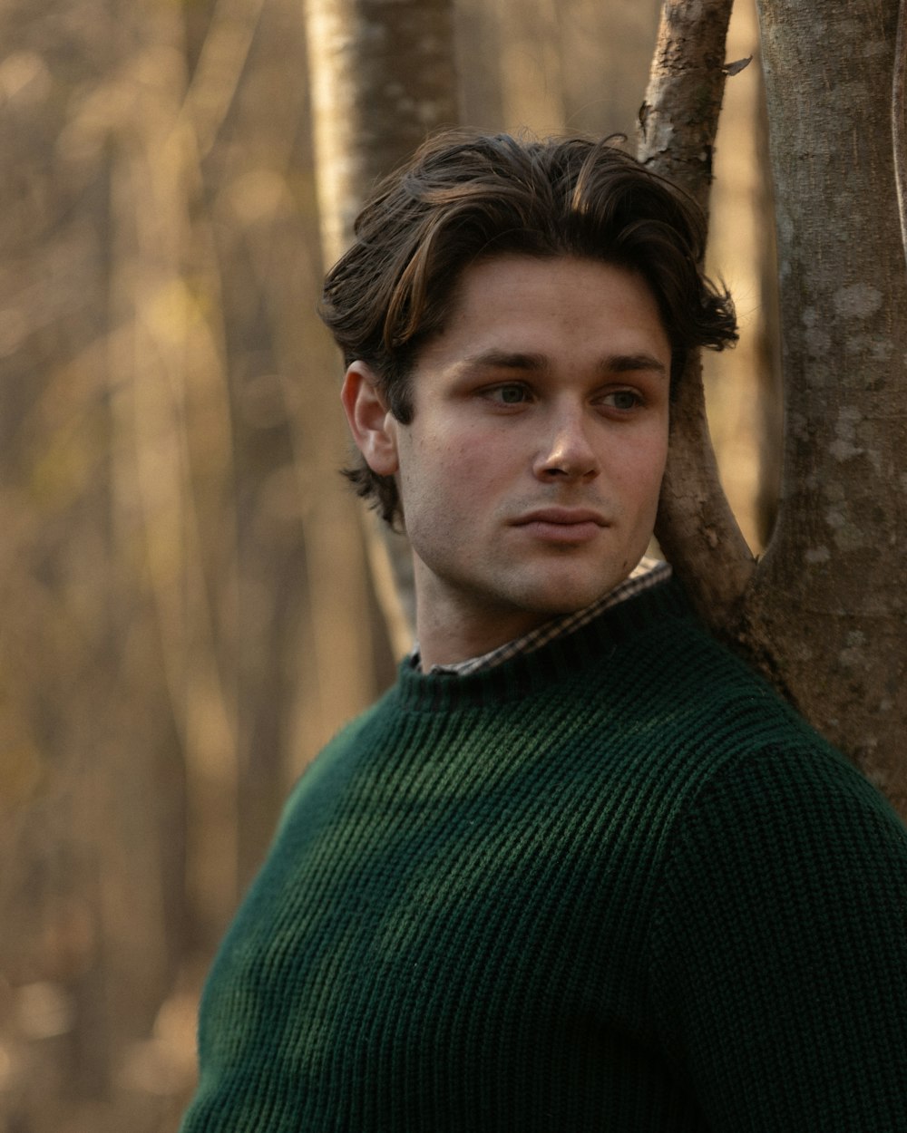 a man in a green sweater standing next to a tree