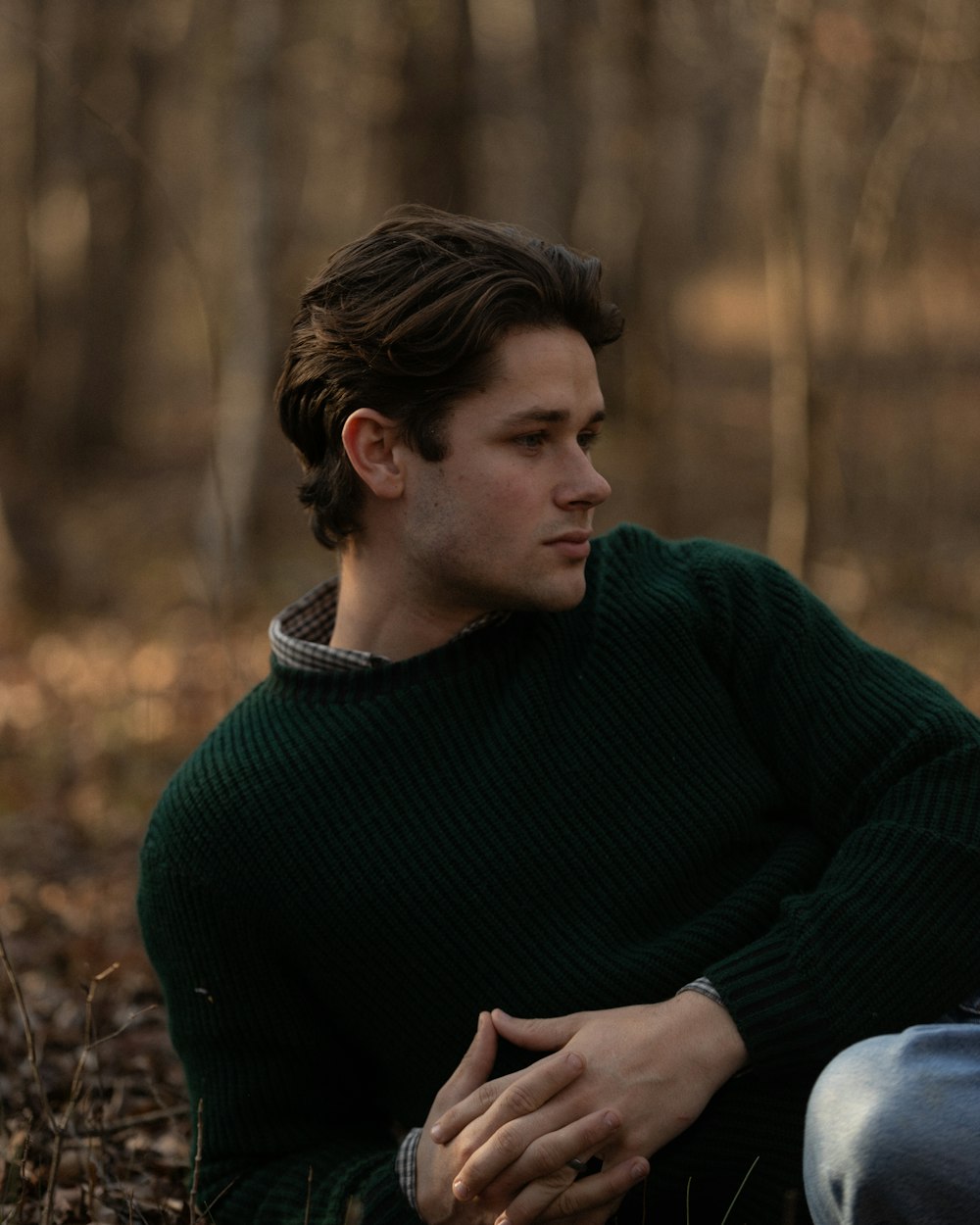 a man in a green sweater sitting in the woods