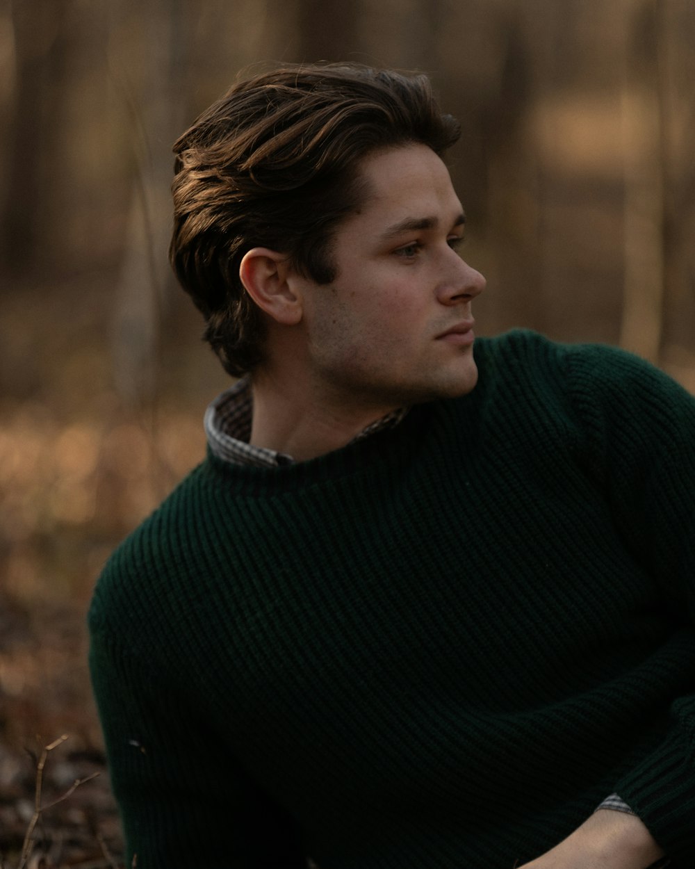 a man in a green sweater sitting in the woods