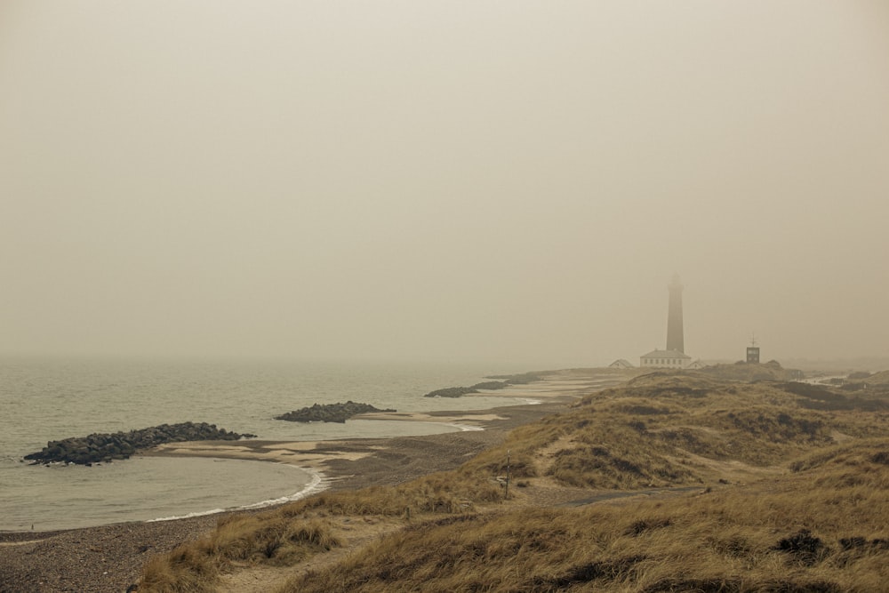 a foggy beach with a lighthouse in the distance