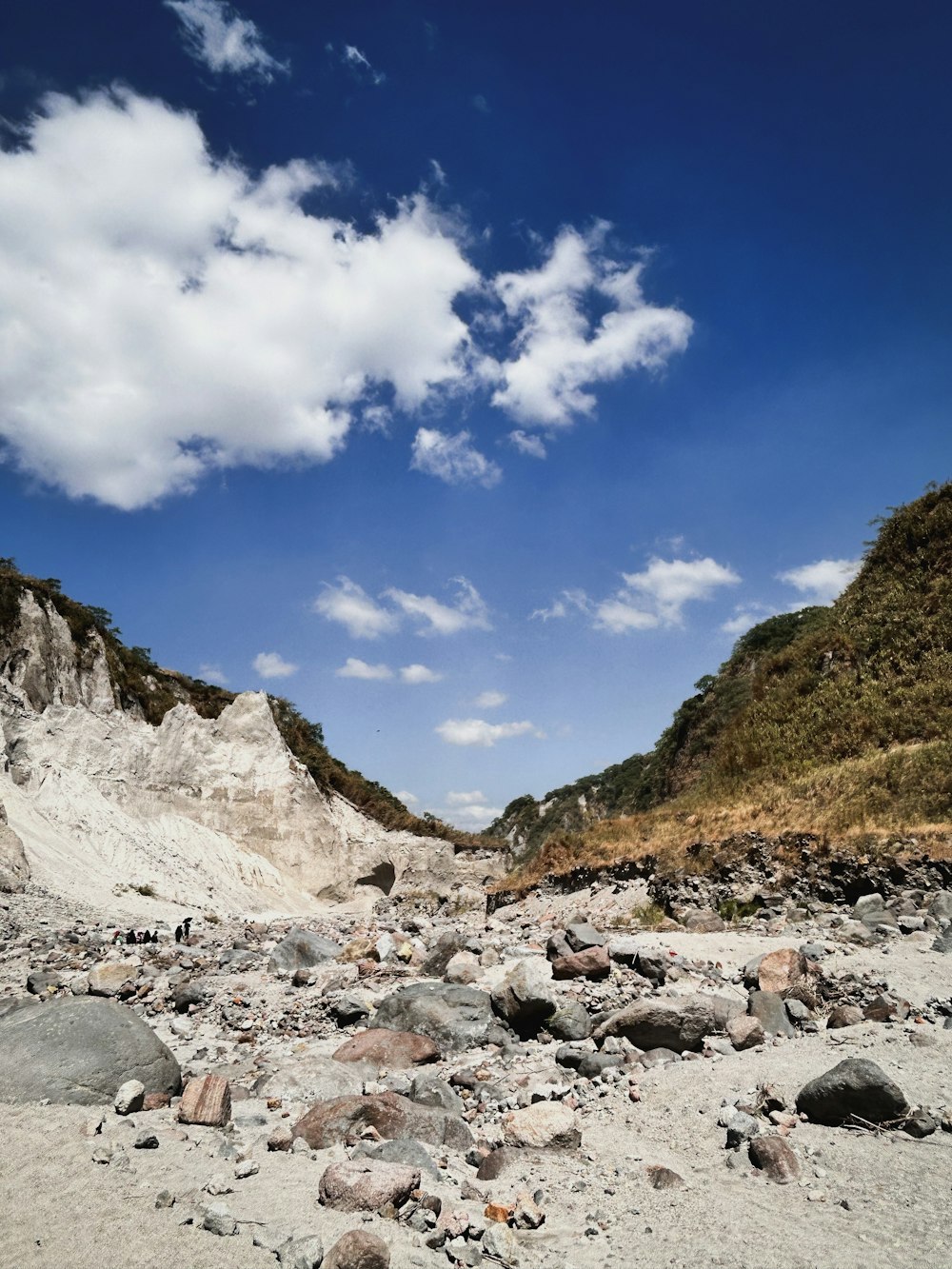 a sandy beach with rocks and a hill in the background