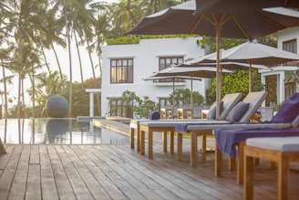 a wooden deck with chairs and umbrellas next to a swimming pool