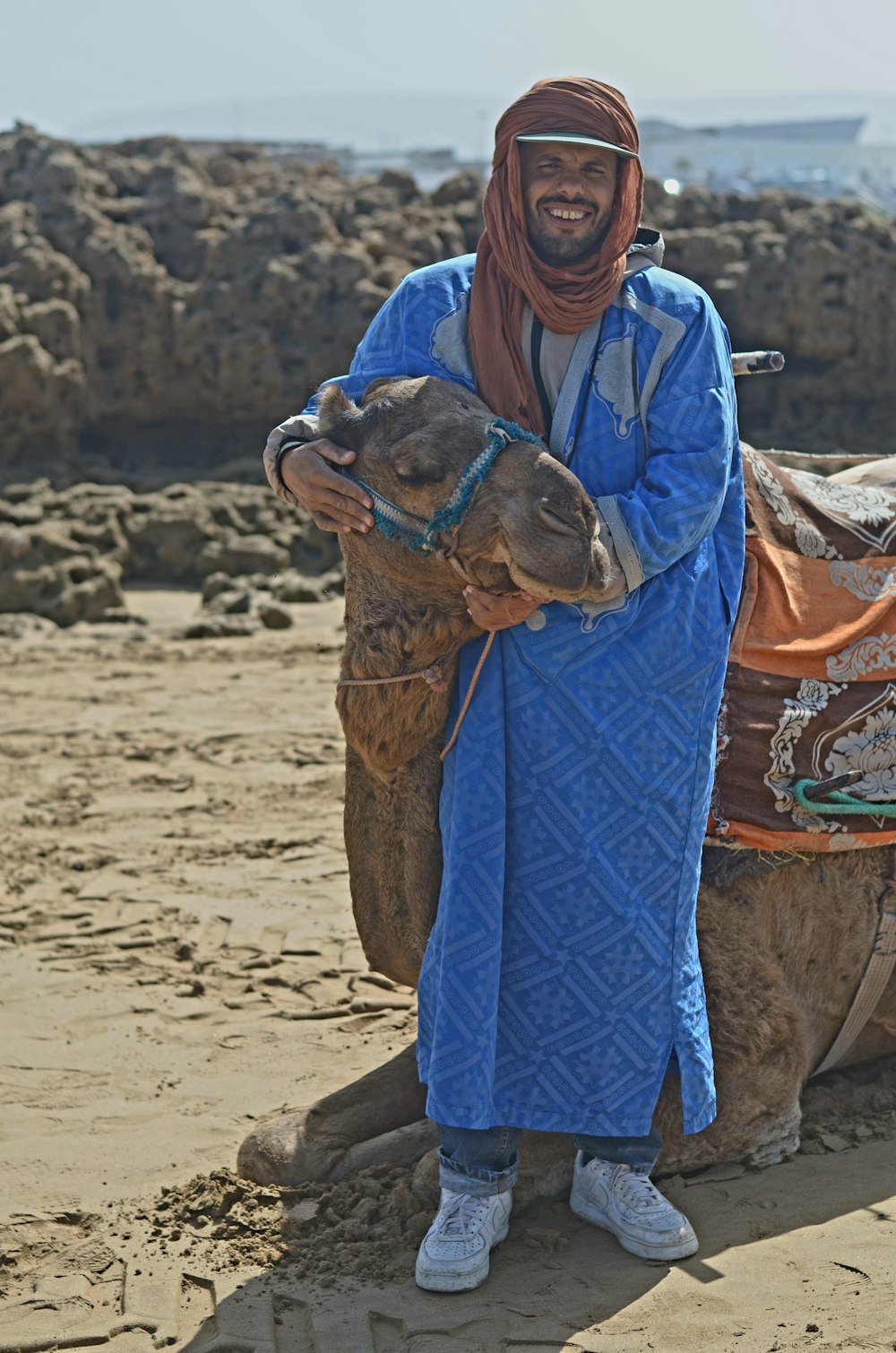 un homme en tenue bleue debout à côté d’un chameau