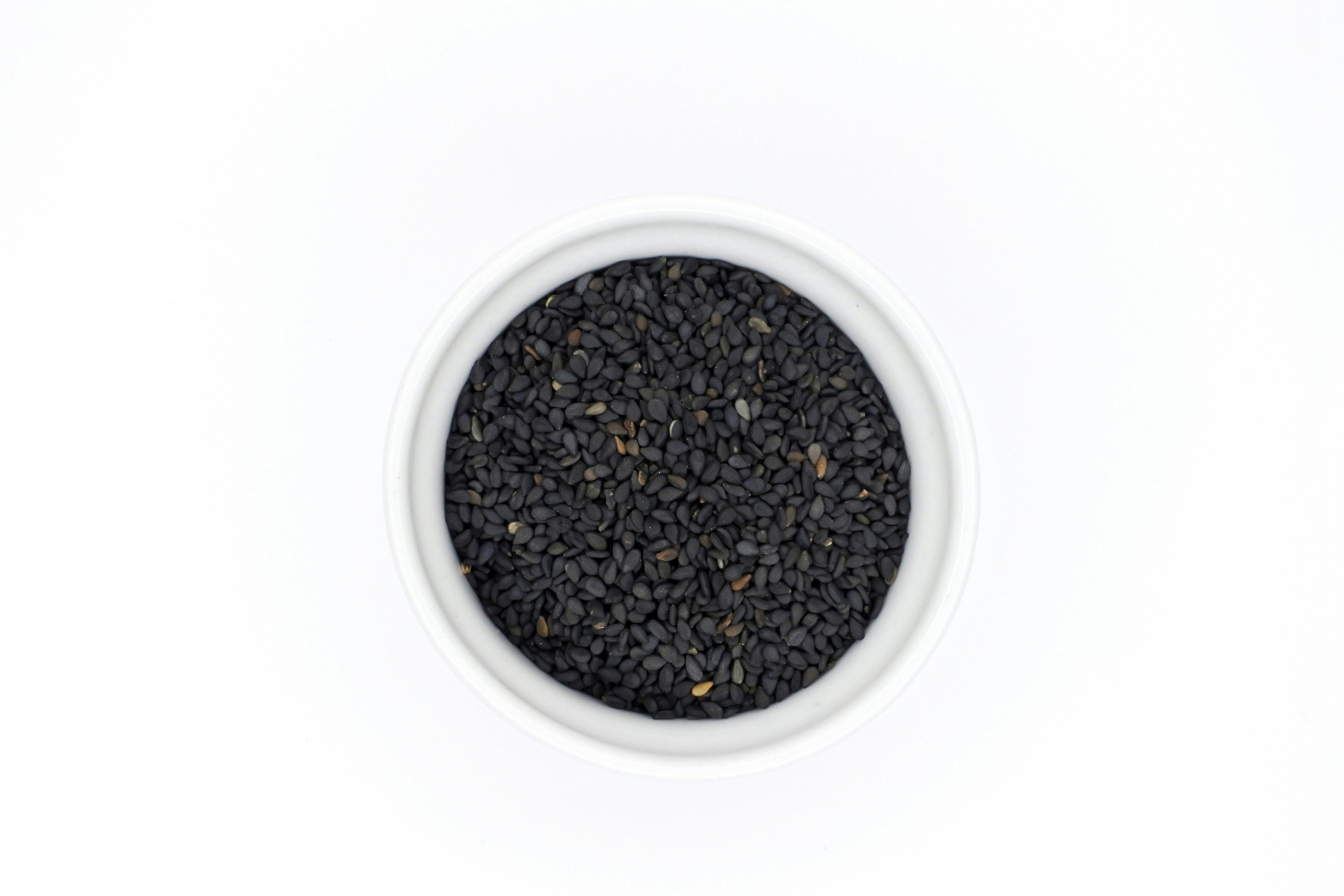 White and black sesame seeds mixed in a small white bowl, natural light
