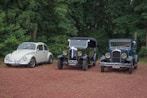 three antique cars parked in a row in front of trees