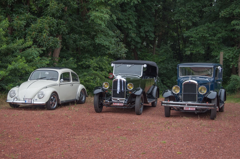 three antique cars parked in a row in front of trees