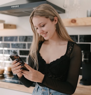 a woman standing in a kitchen looking at her cell phone