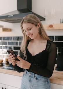 a woman standing in a kitchen looking at her cell phone