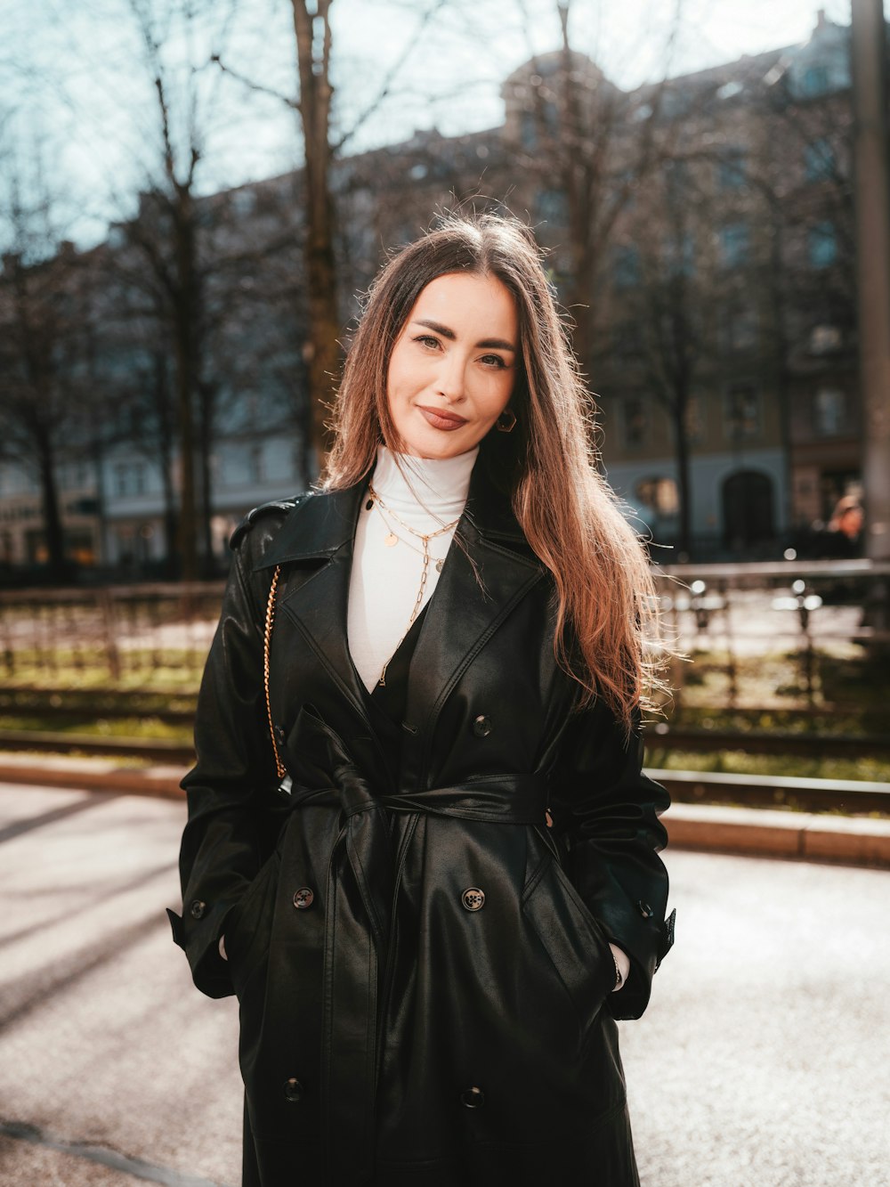 a woman in a black trench coat standing on a street