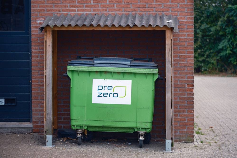 a green trash can sitting in front of a brick building