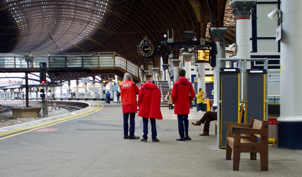 赤いジャケットを着た2人が電車のプラットホームに立つ