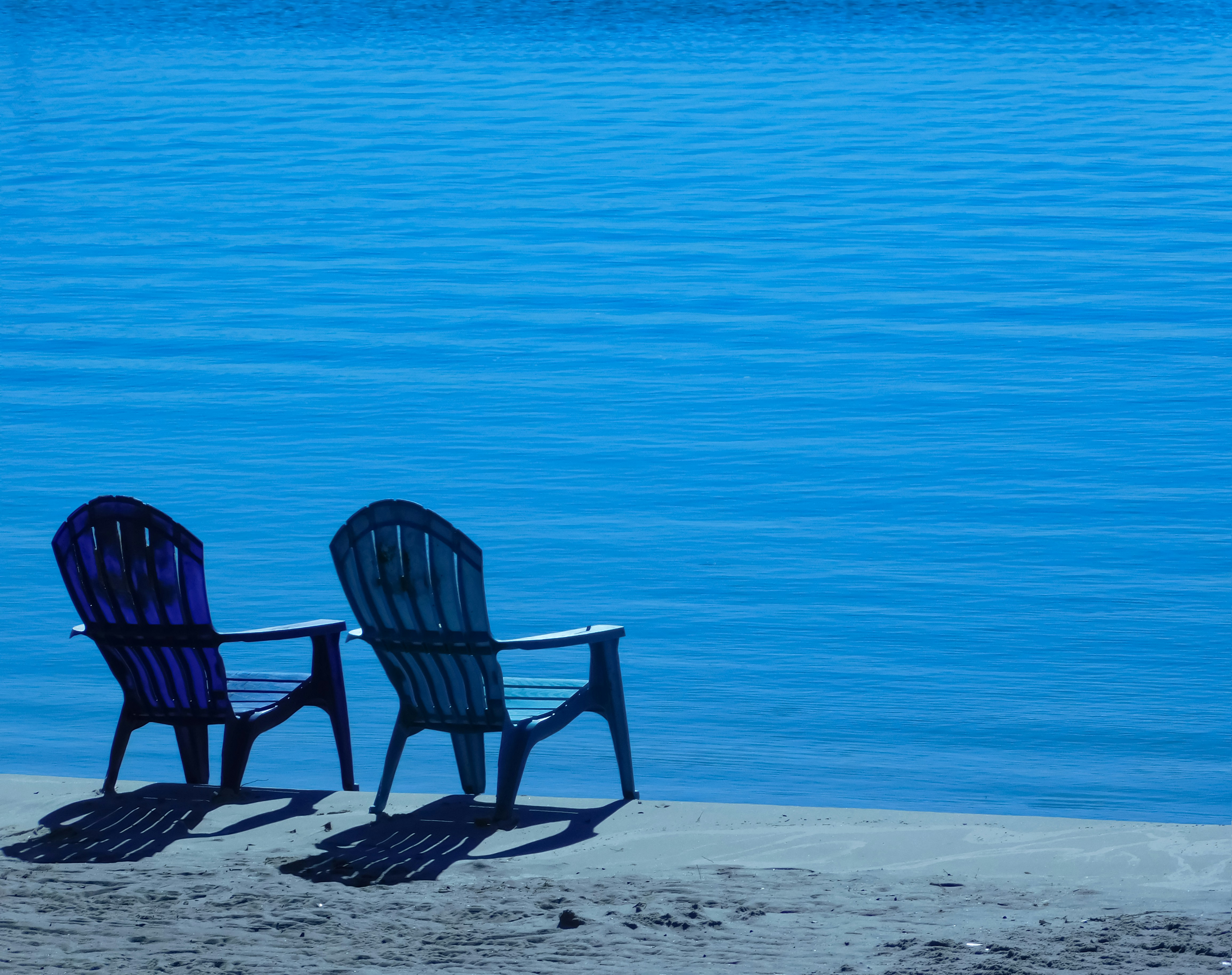a couple of chairs sitting on top of a sandy beach, 