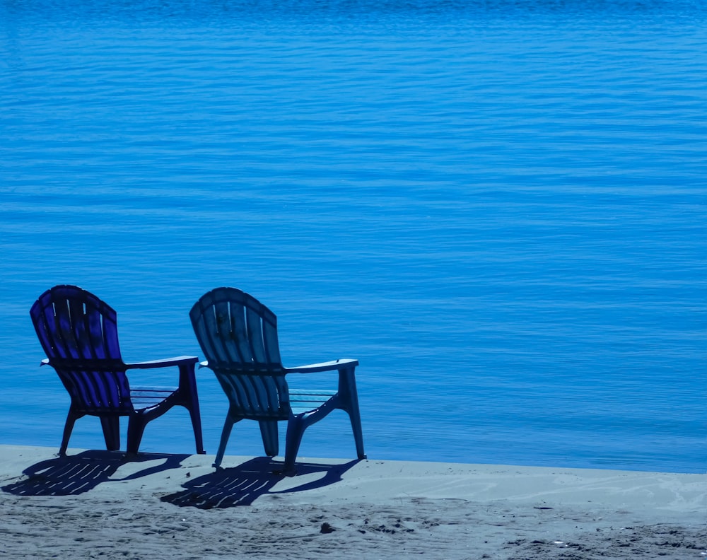 a couple of chairs sitting on top of a sandy beach