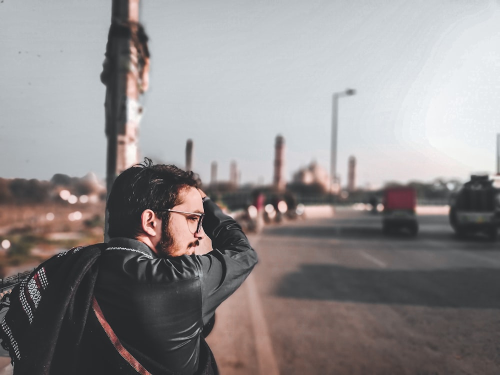 a man in a black jacket is standing on the side of the road