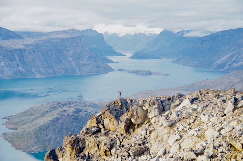 a man standing on top of a mountain next to a lake