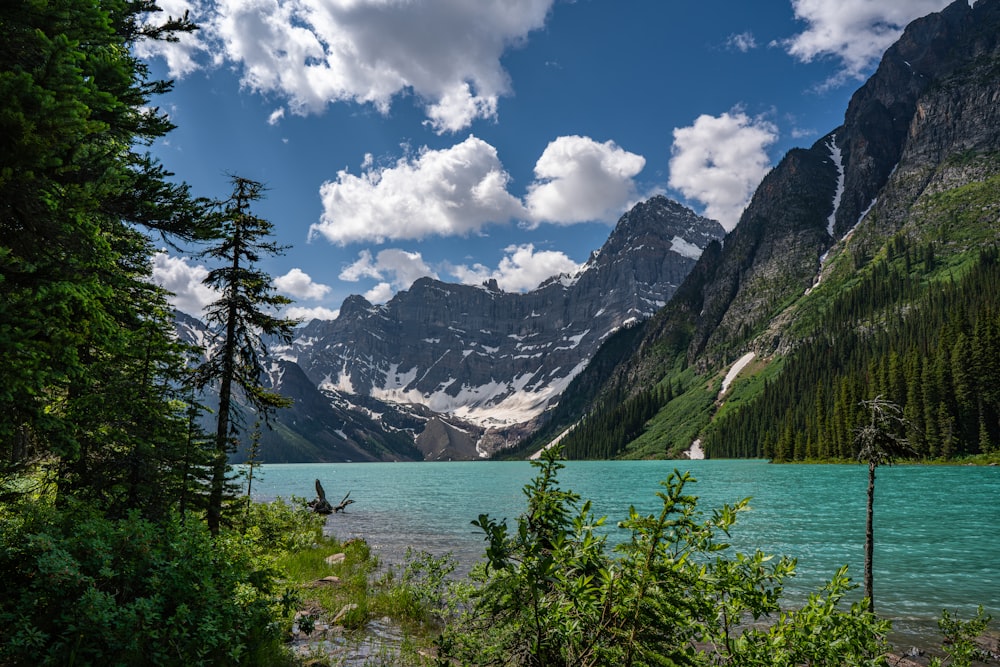 a lake surrounded by trees and mountains under a cloudy sky