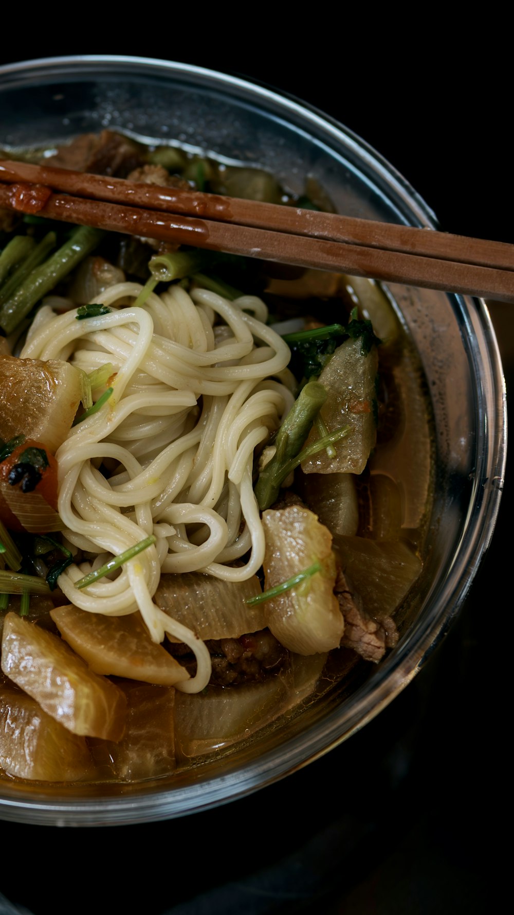 a bowl of noodles and vegetables with chopsticks