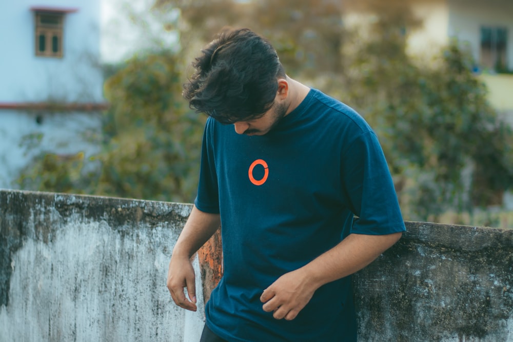 a man leaning against a wall looking down at his cell phone