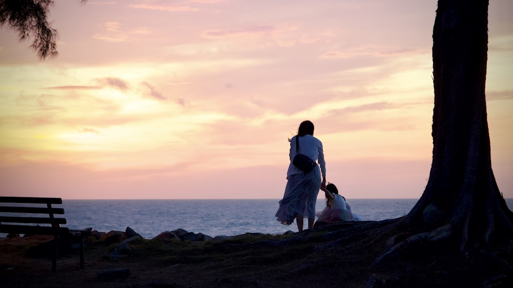 a woman standing next to a tree next to the ocean