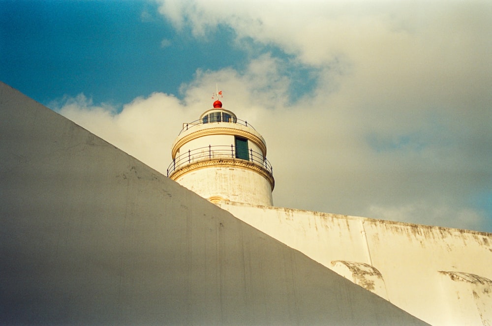 a white lighthouse with a red top on a cloudy day