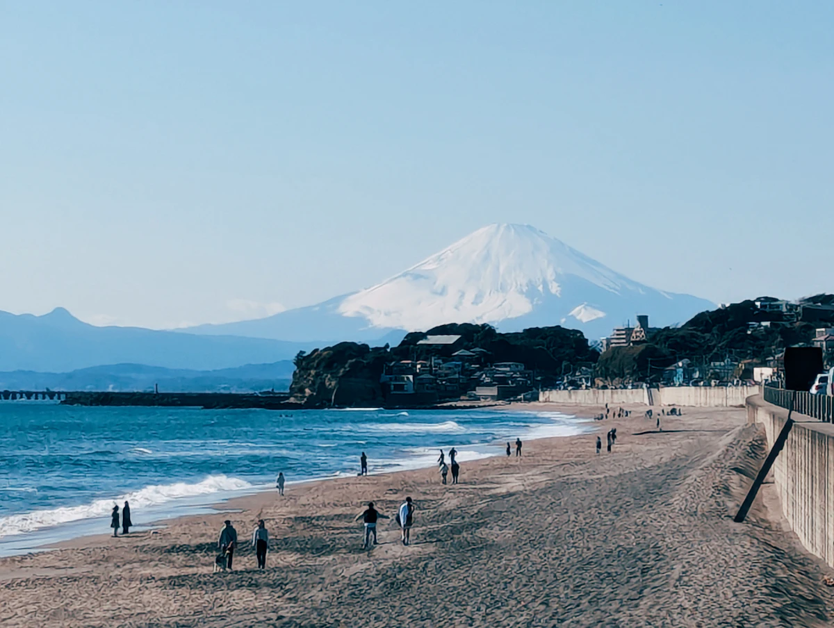 A surfer walks along the Shonan coast with Mount Fuji in the background