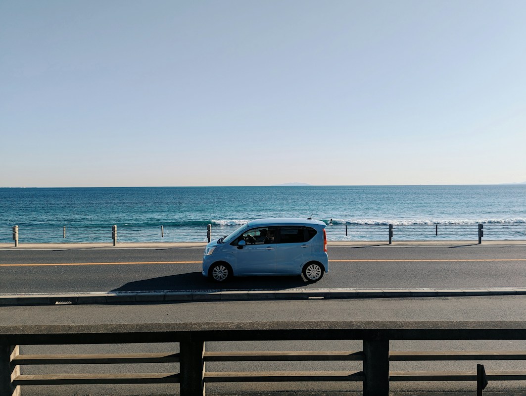 小型車行駛在海岸公路上，右側是開闊海面