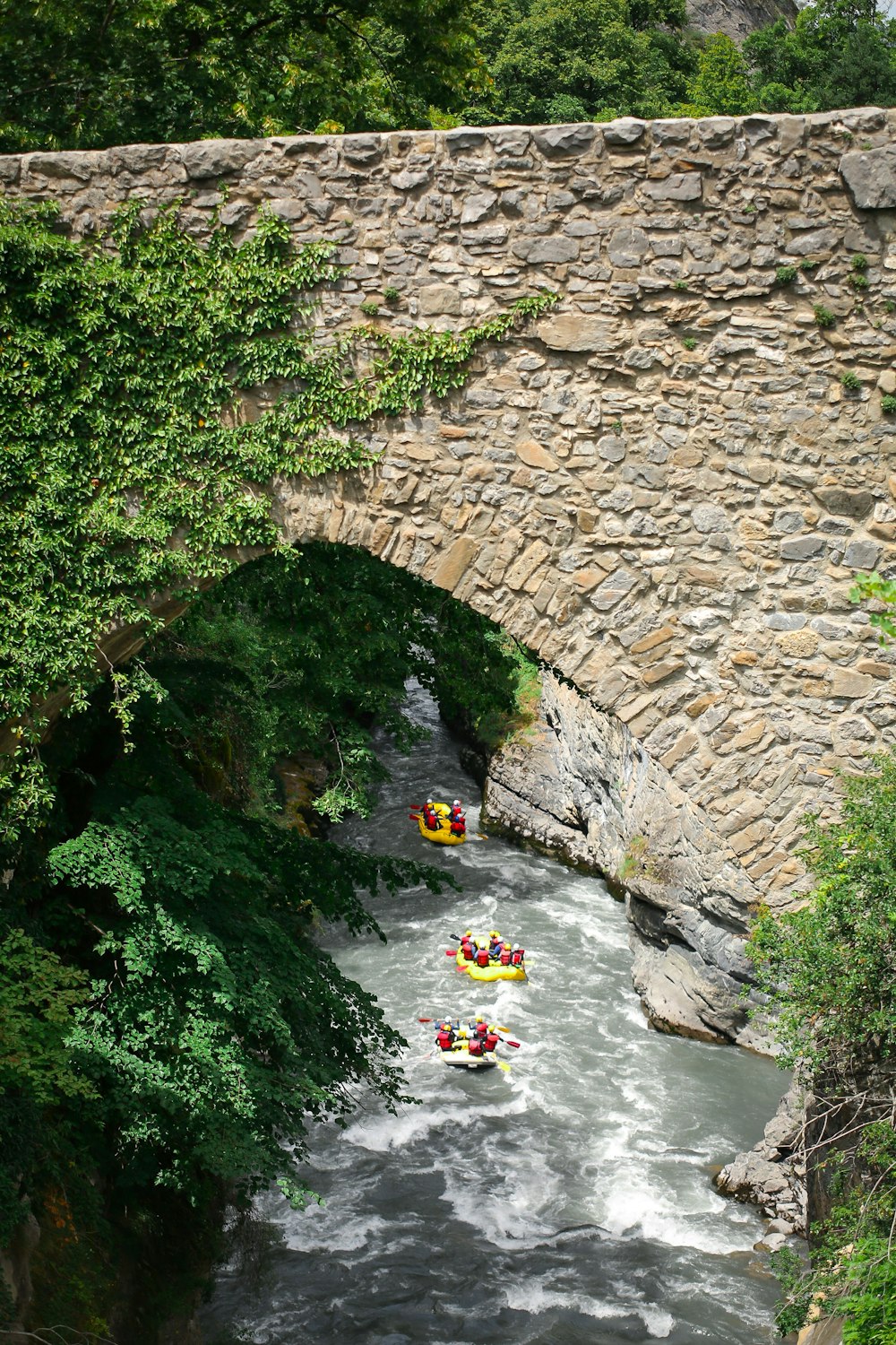 a group of people on rafts going under a stone bridge