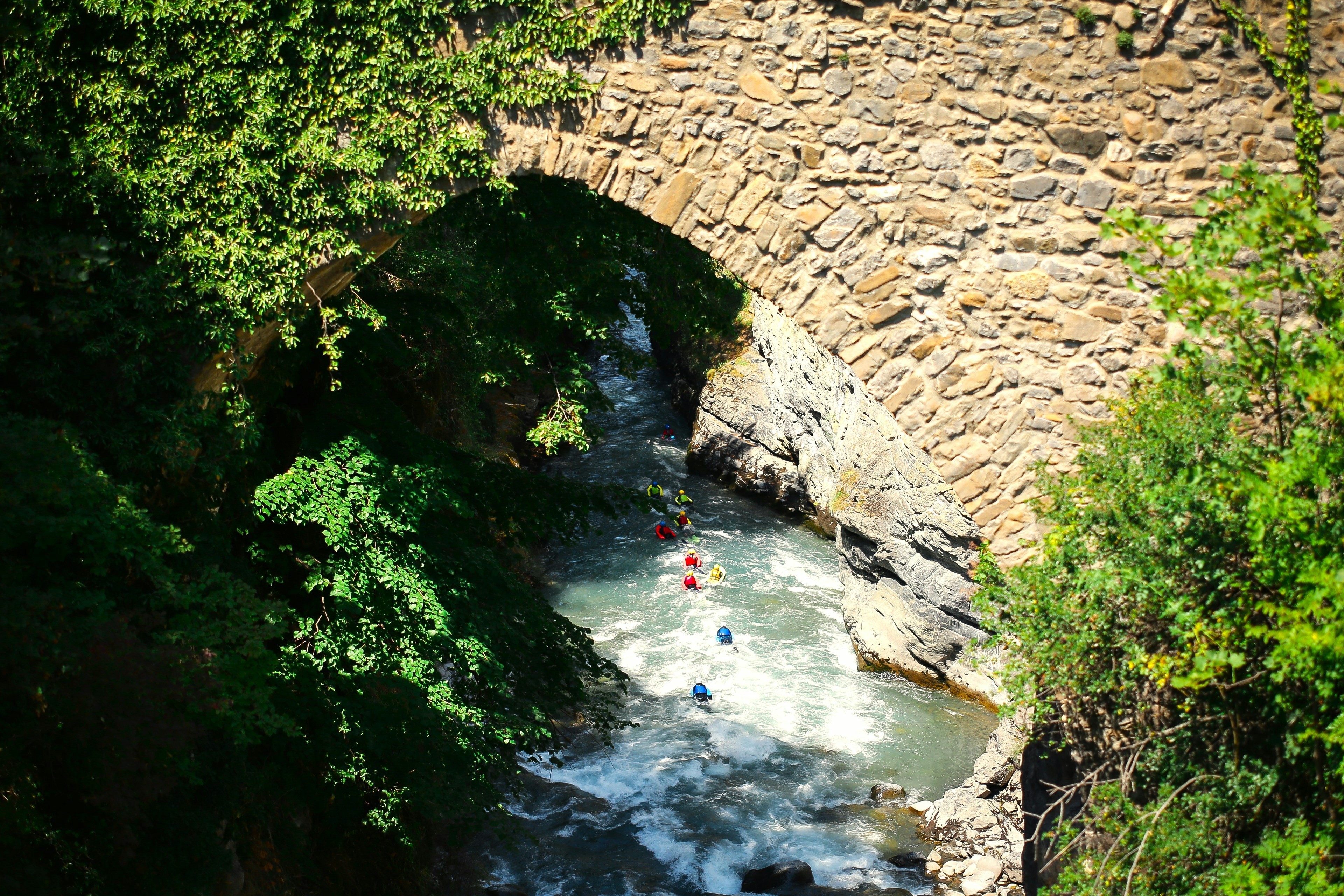 a group of people riding kayaks down a river under a bridge, nage en eau vive sur l