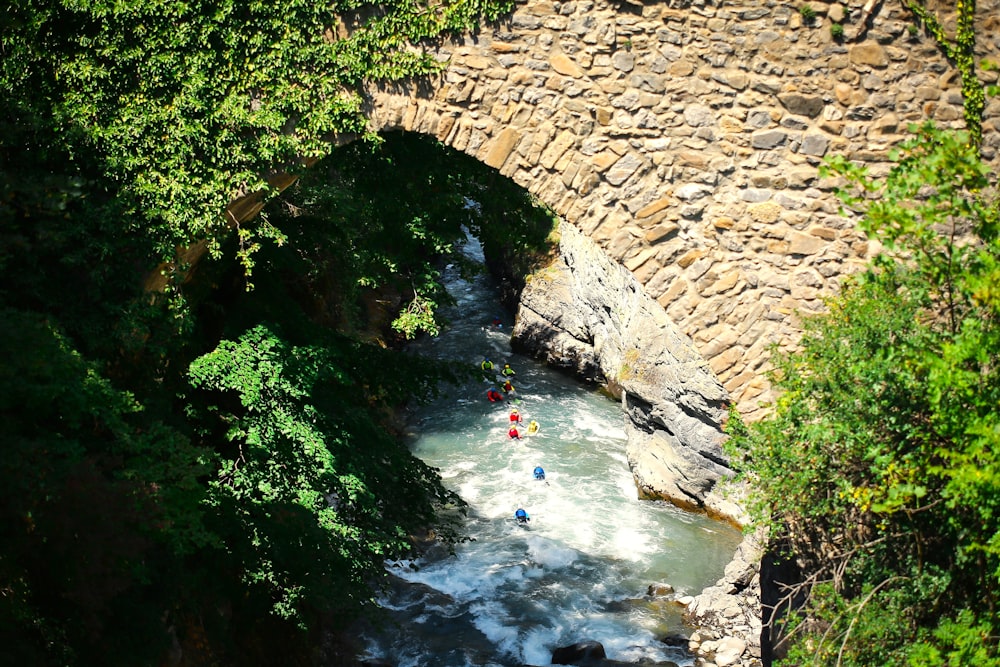 a group of people riding kayaks down a river under a bridge