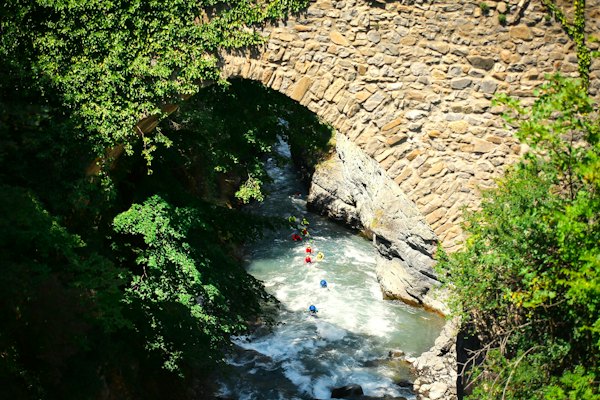 A group of people riding kayaks down a river under a bridge — Kuldīga, Latvia