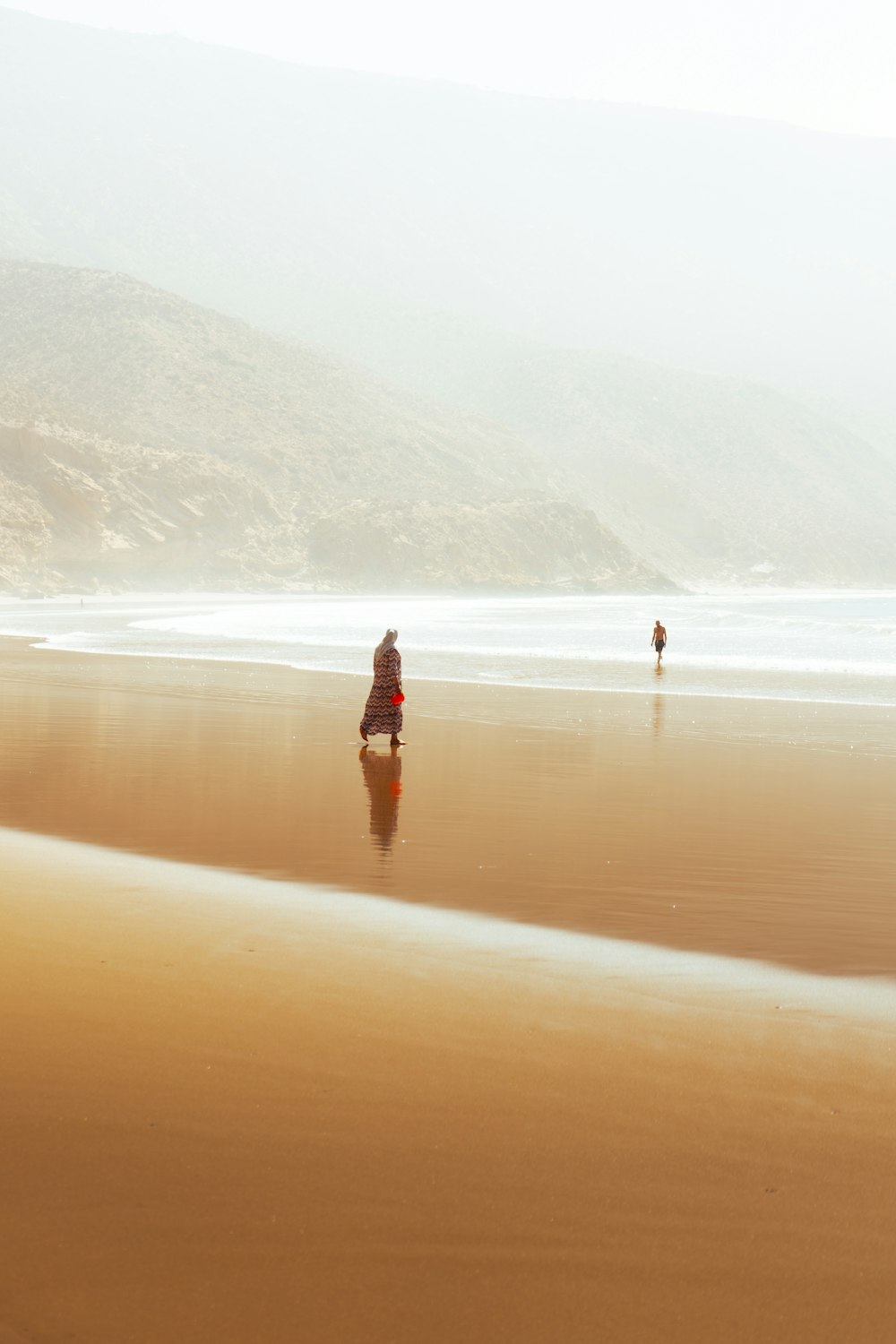 a couple of people walking across a sandy beach