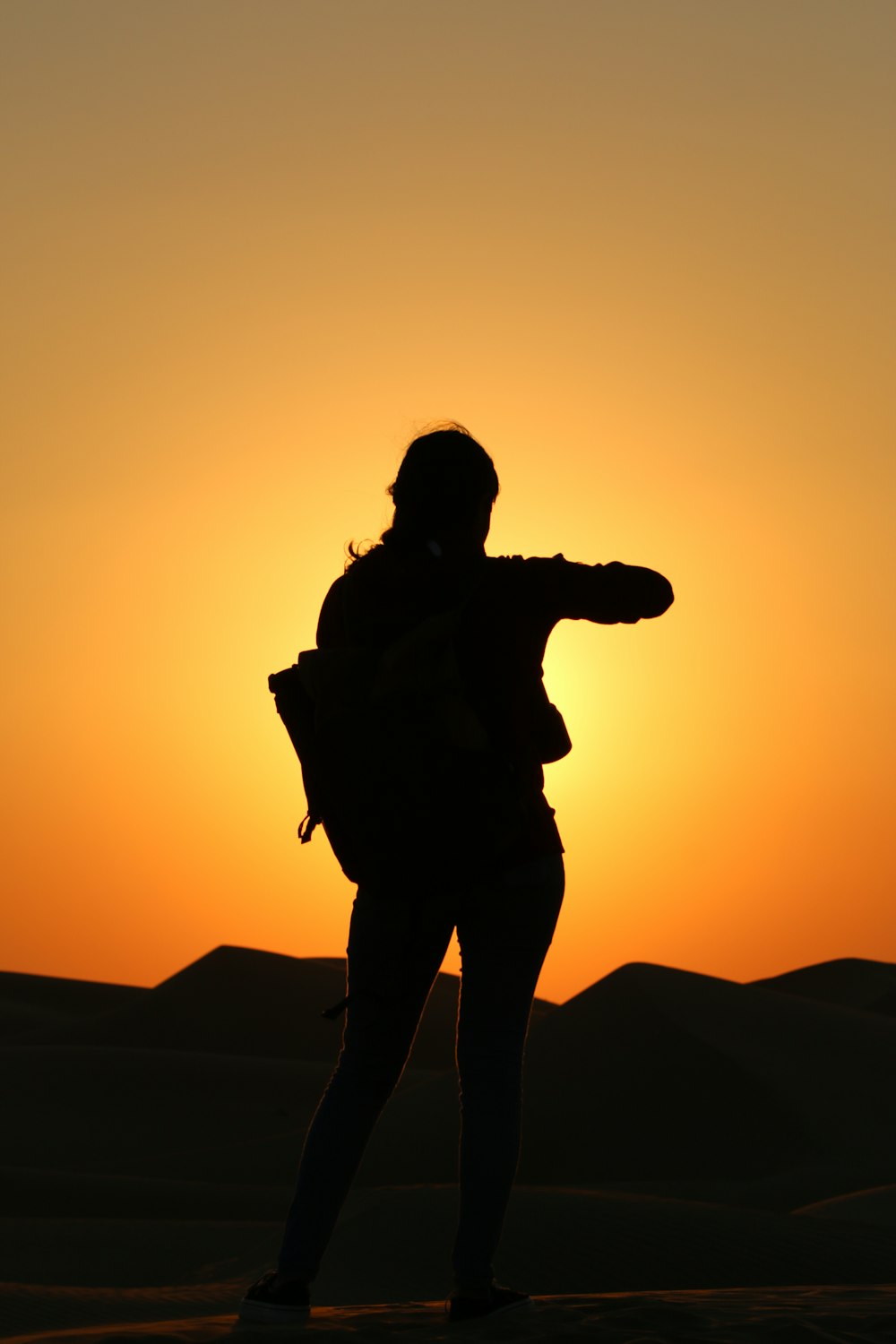 a woman standing in the middle of a desert at sunset