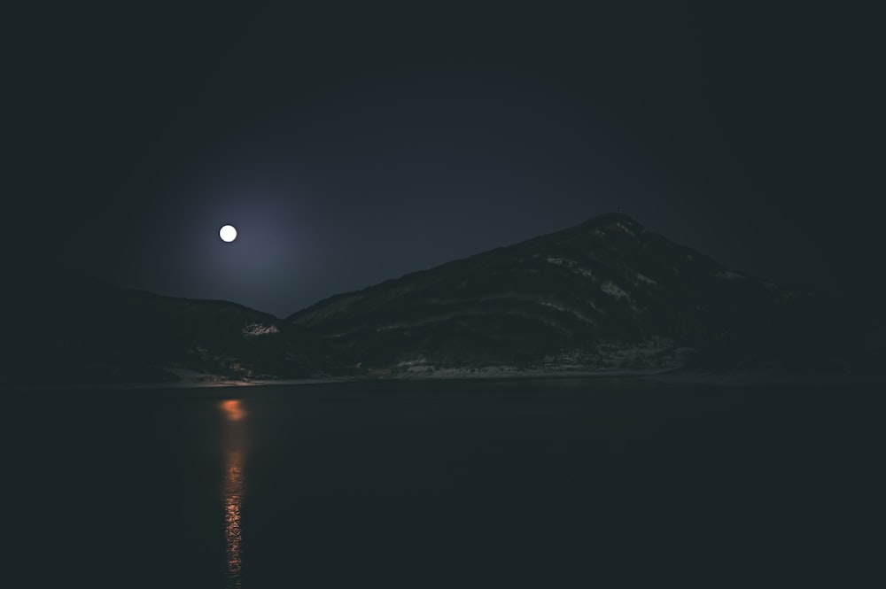 Se ve una luna llena sobre una montaña por la noche