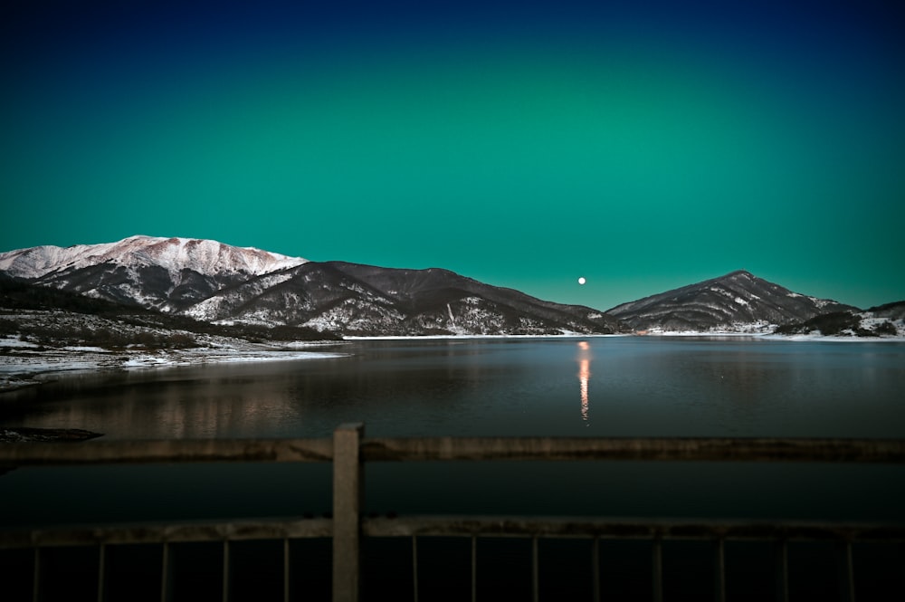 a lake surrounded by snow covered mountains under a green sky