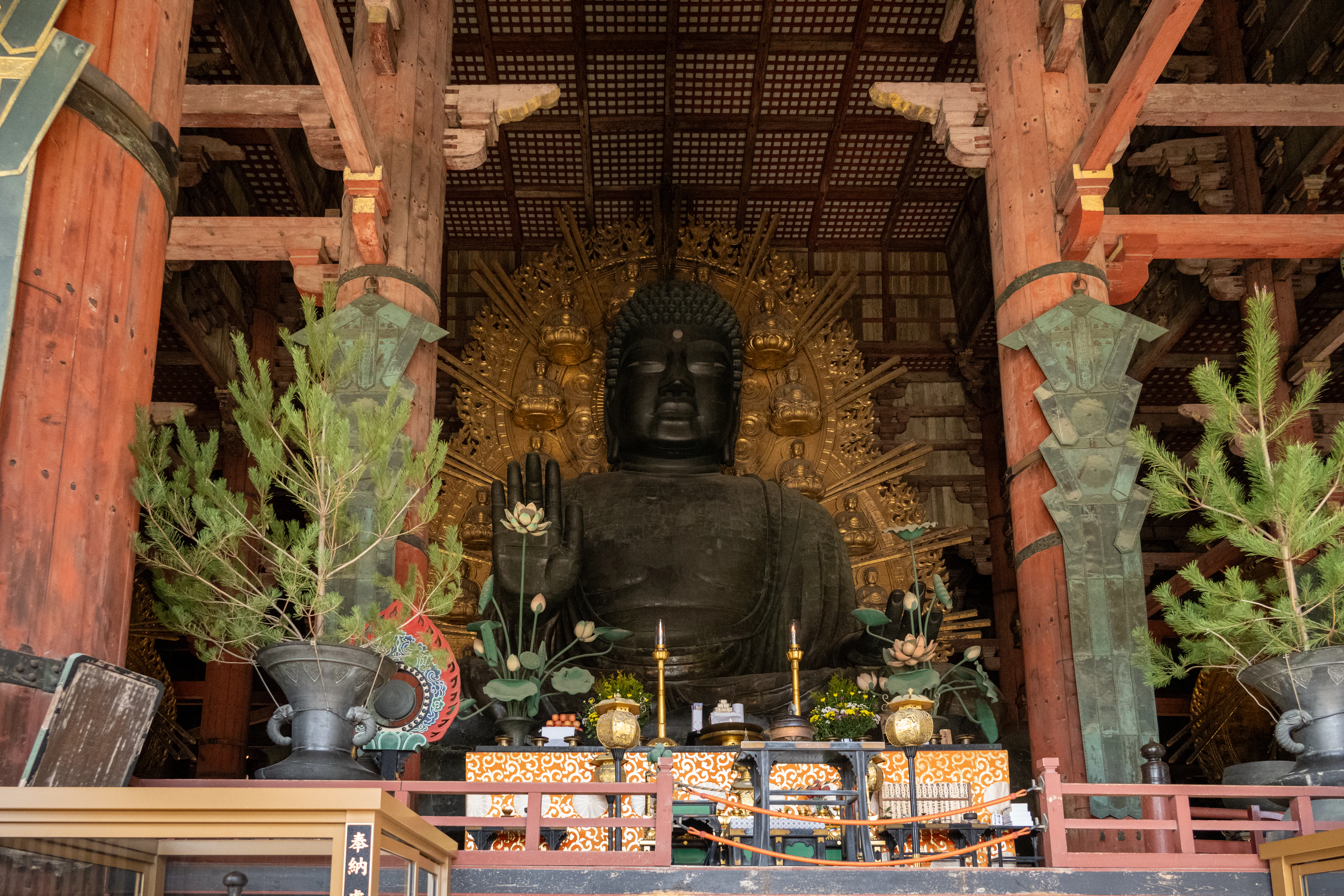 The great bronze Buddha of Todai-ji seated beneath its gilded halo inside the vast wooden Daibutsuden hall in Nara, with bronze lotus vases and offering vessels on the altar below
