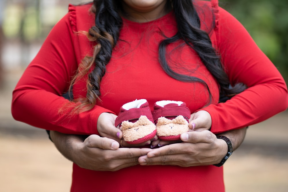 a woman in a red dress holding a pair of baby shoes