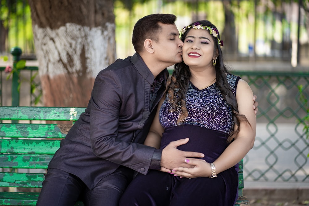 a pregnant couple sitting on a green bench
