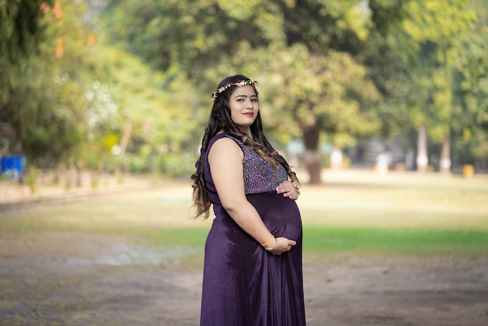 a pregnant woman in a purple dress poses for a picture
