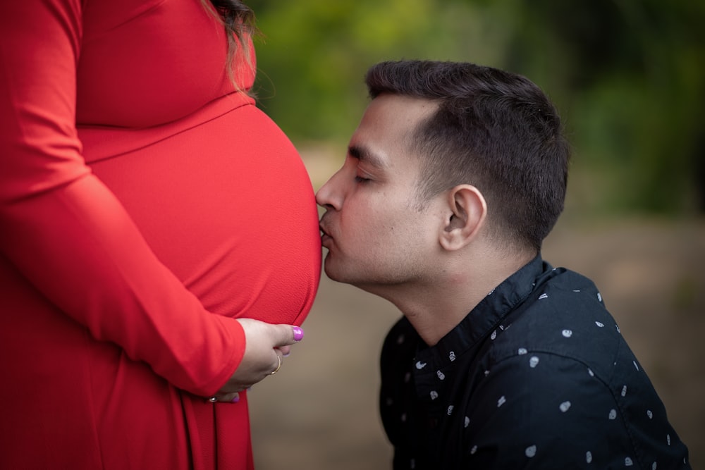 a pregnant man kissing a pregnant woman's belly